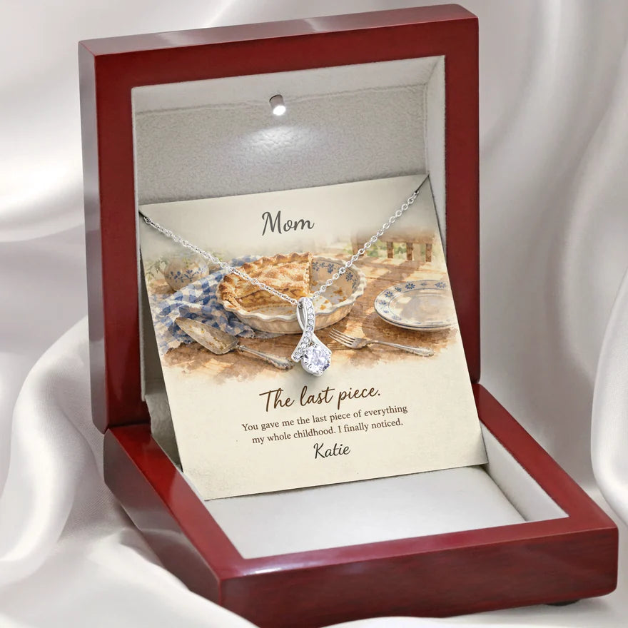 The open mahogany gift box with its light on: a printed card reading Mom, The last piece, with a silver necklace resting on it